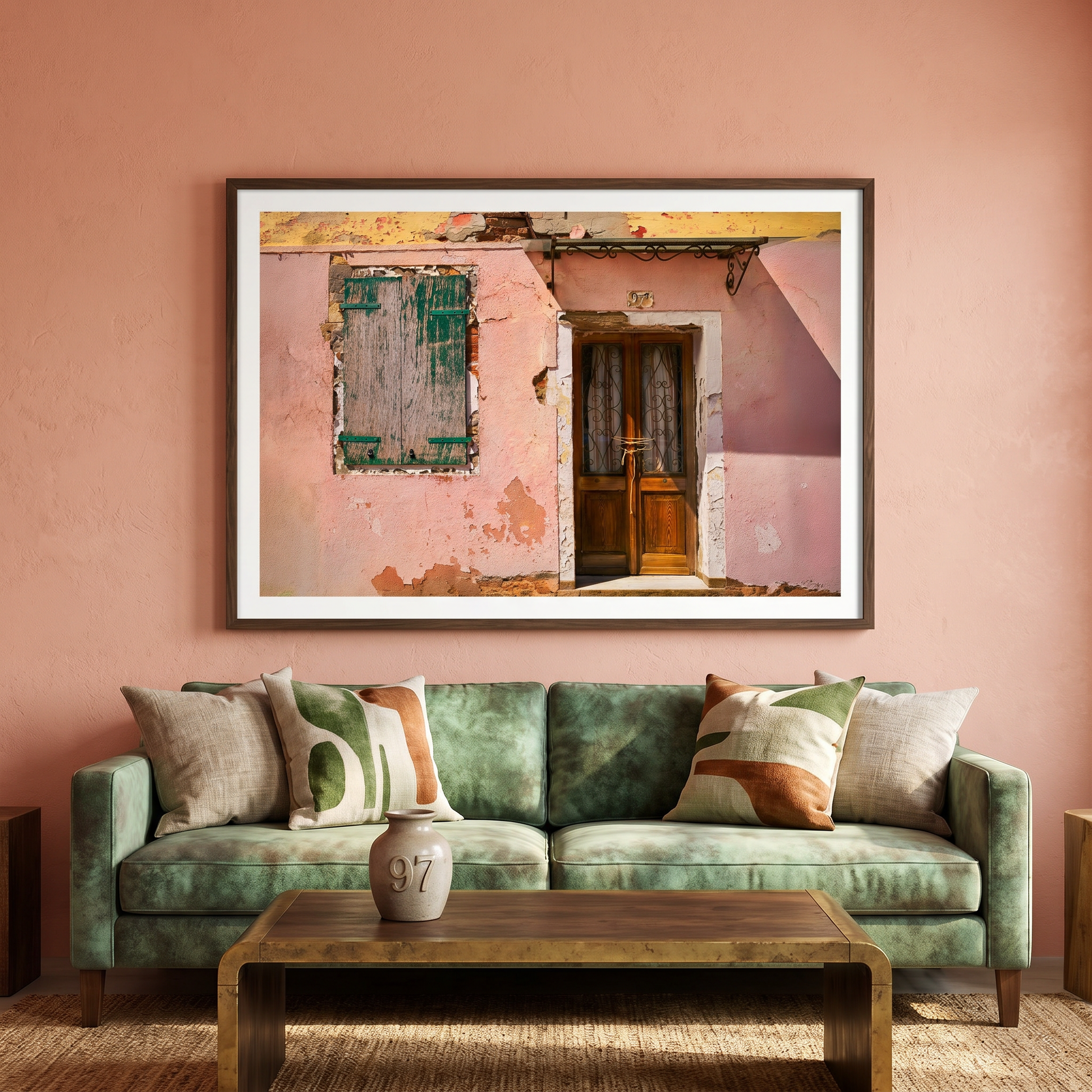Framed artwork of a pink building on a peach wall above a green sofa with decorative pillows.