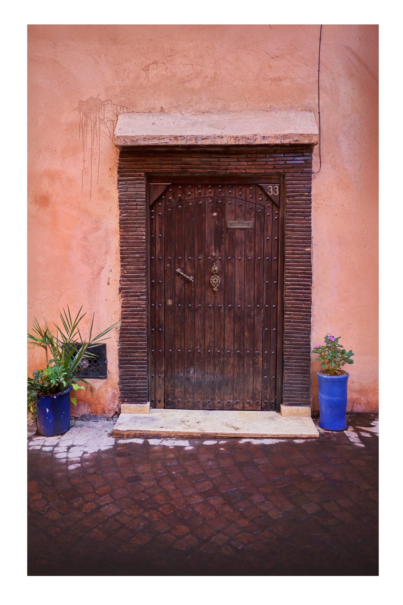 Wooden door with decorative patterns on a stone wall with two potted plants. Marrakesh Morocco