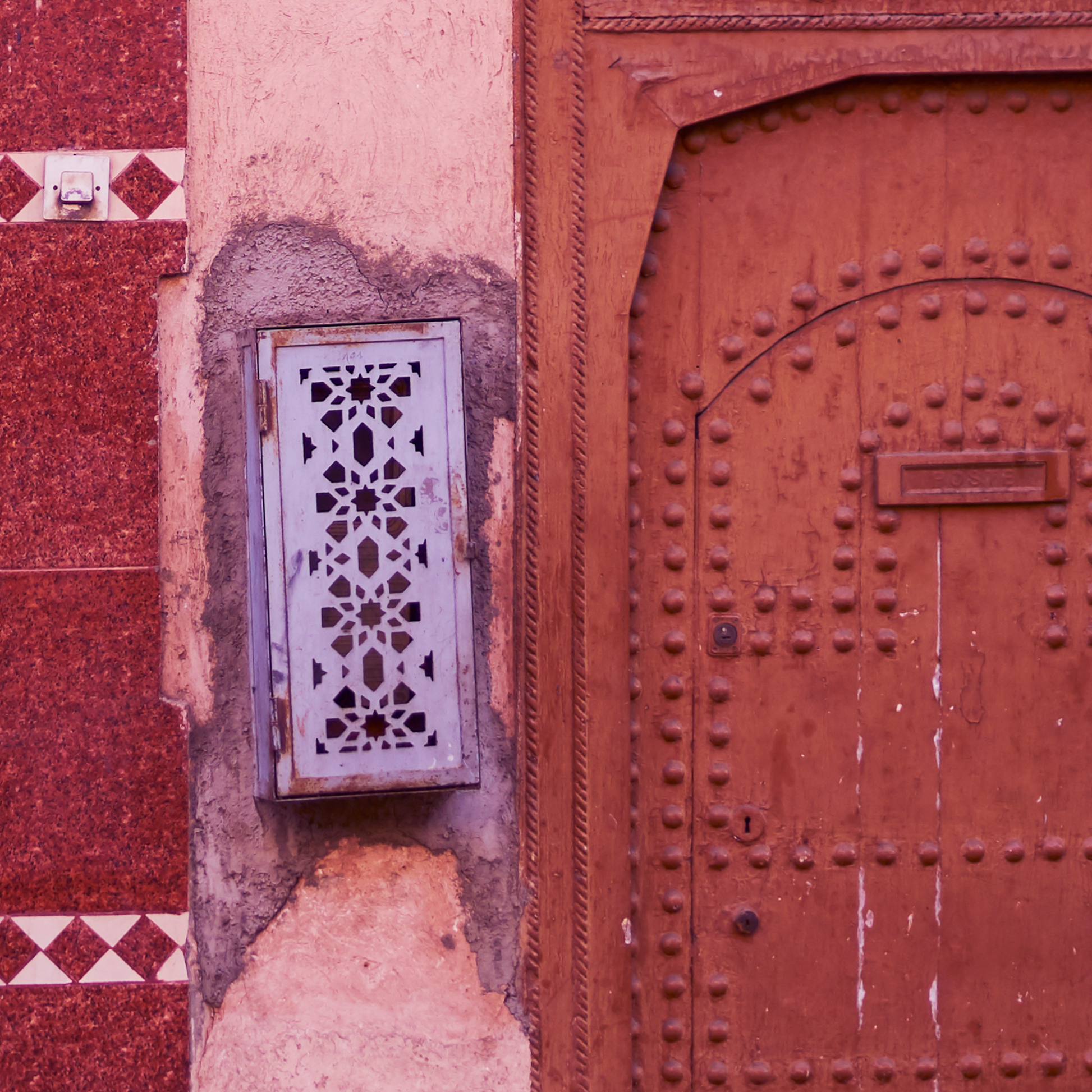 Decorative metal grille on a red wall with an ornate wooden door.