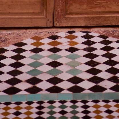 Checkered tile floor with a pattern of black, white, and green tiles, against a wooden door.