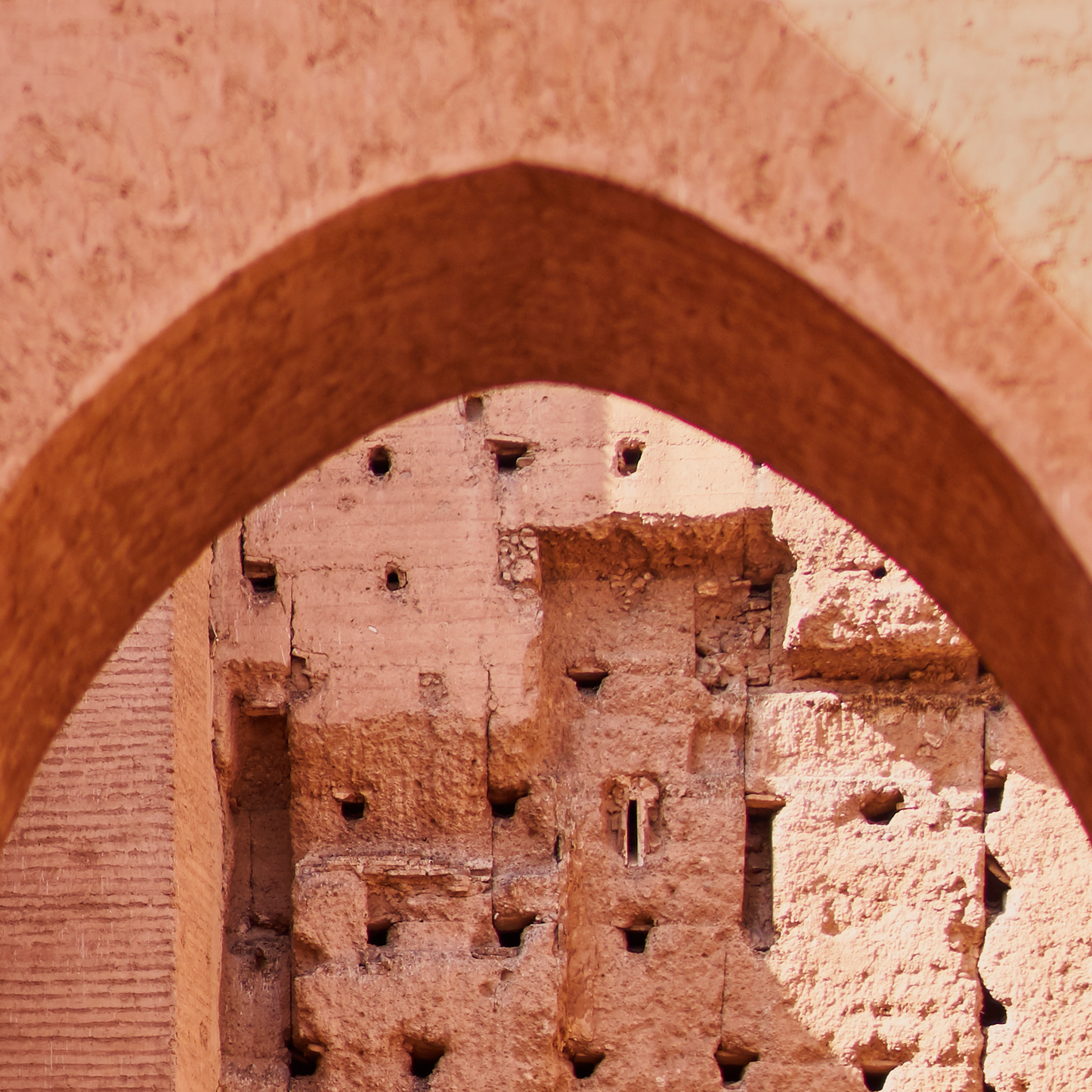 Archway leading to a textured wall with arched niches in a warm-toned color.