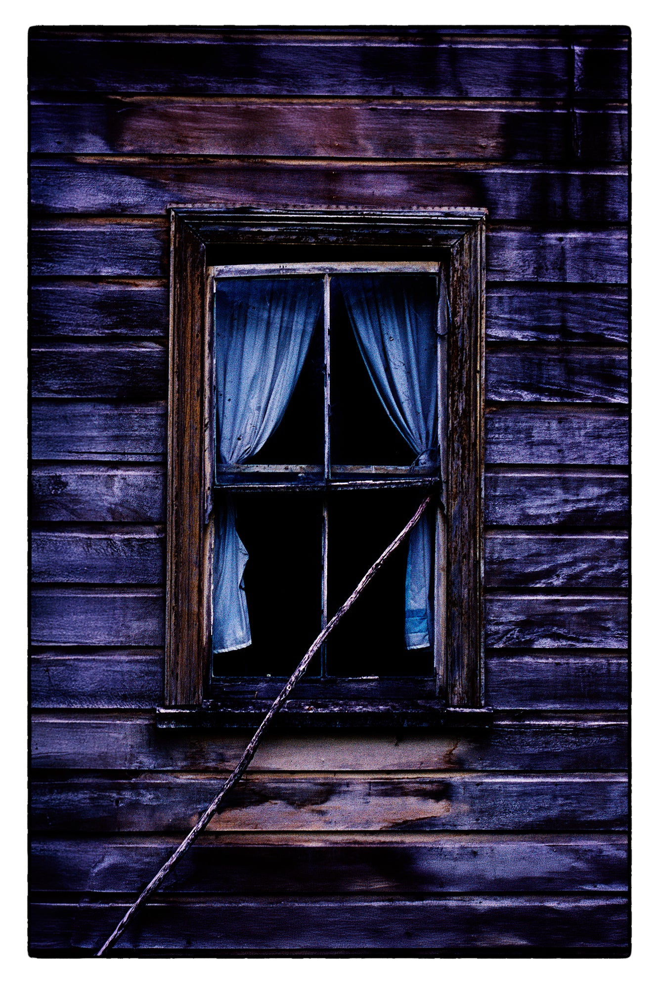 Window with curtains in a wooden cottage setting, evoking a sense of mystery.