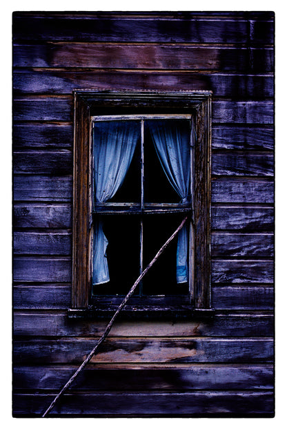 Window with curtains in a wooden cottage setting, evoking a sense of mystery.
