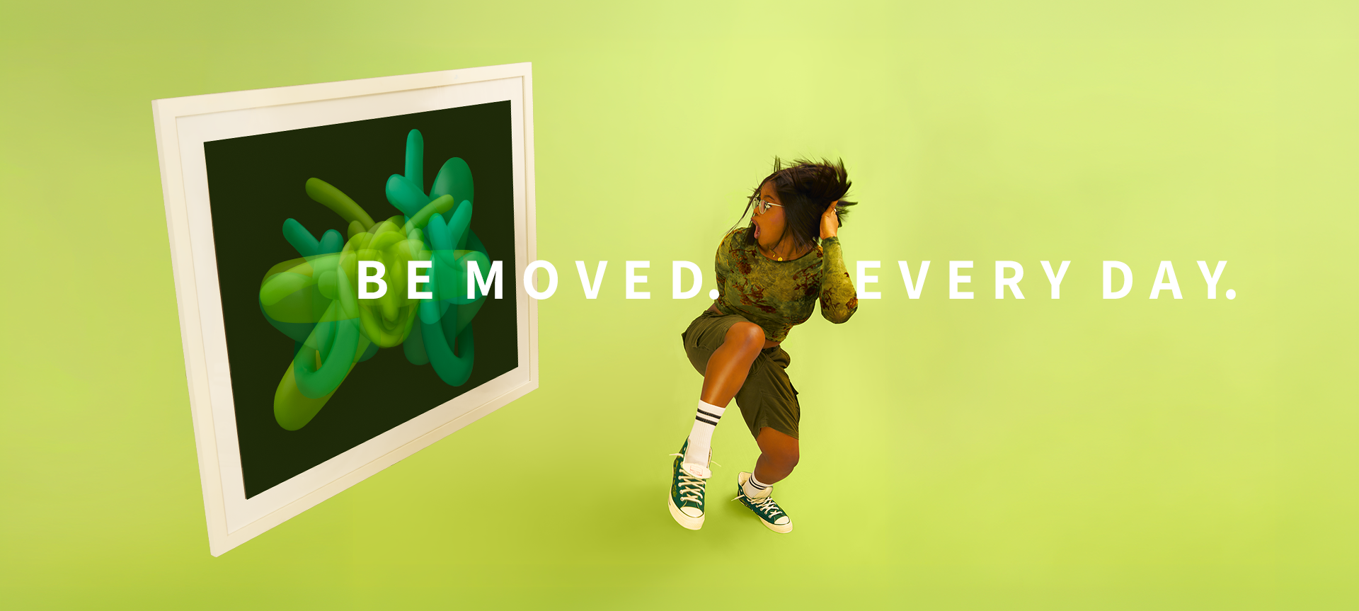 A beautiful woman  in a camouflage long-sleeve top, olive shorts, white socks, and green sneakers poses next to a large framed abstract art print featuring green and teal shapes on a dark background. The scene is set against a solid light green wall with the text 'BE MOVED. EVERY DAY.