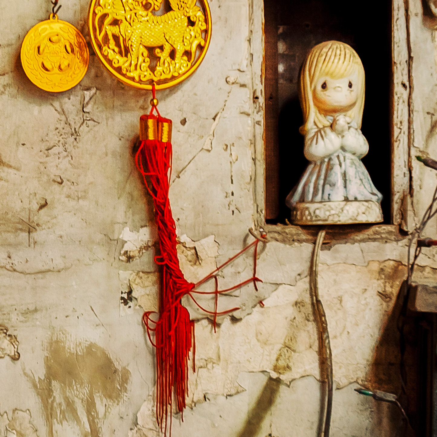 Decorative items including a gold circular ornament, red tassel, and a small figurine on a textured wall.