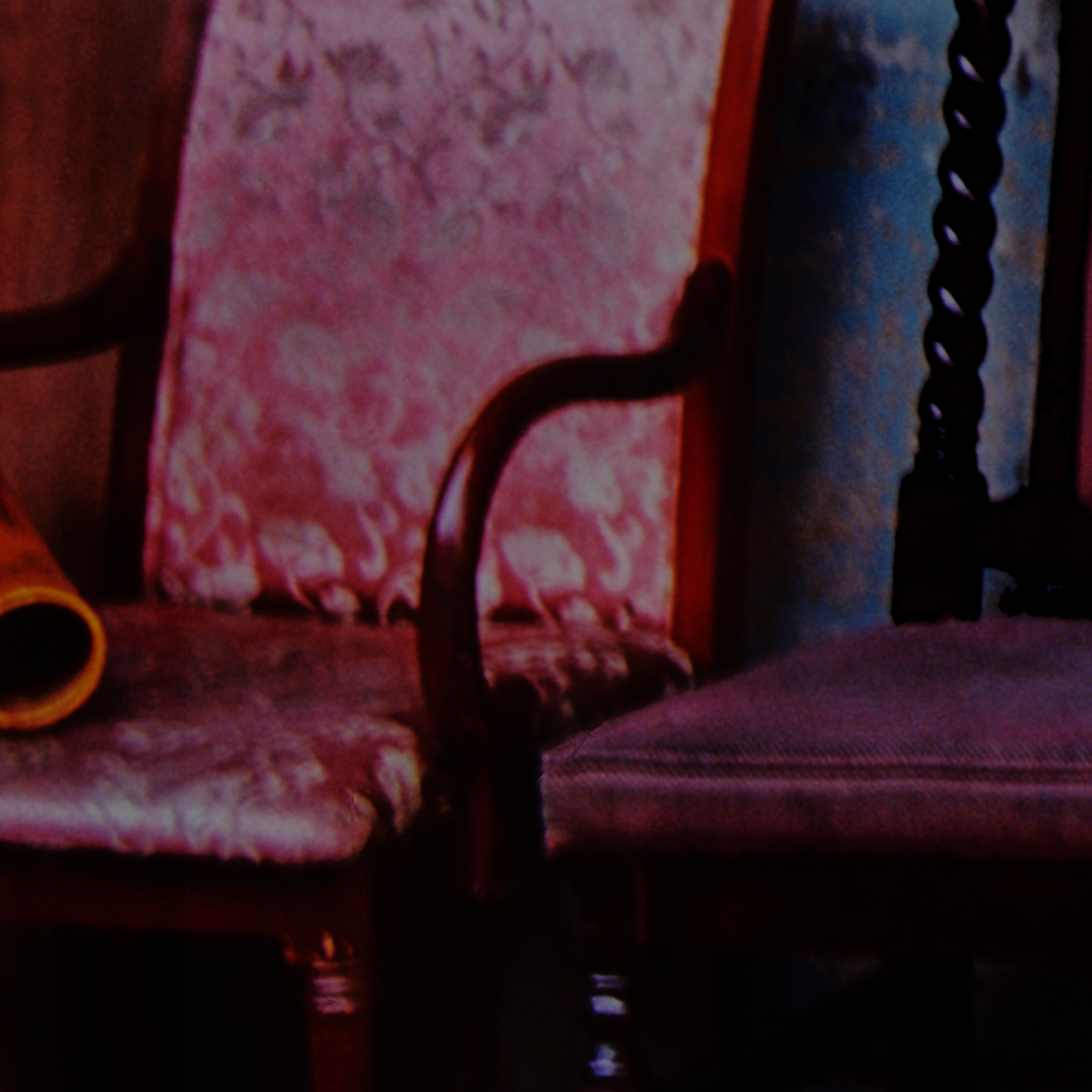 Close-up of a wooden chair with a patterned cushion against a floral wallpapered wall.