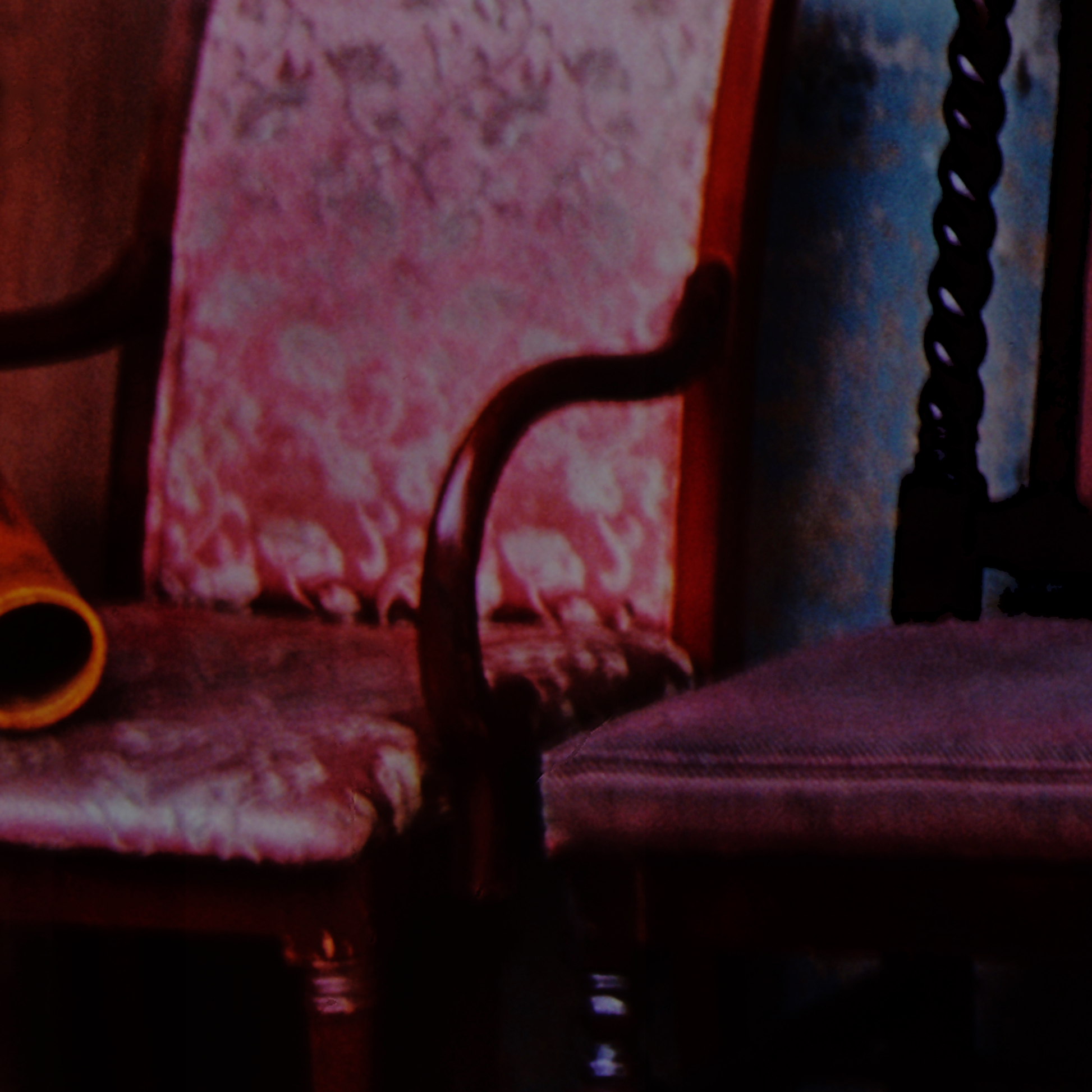 Close-up of a wooden chair with a patterned cushion against a floral wallpapered wall.