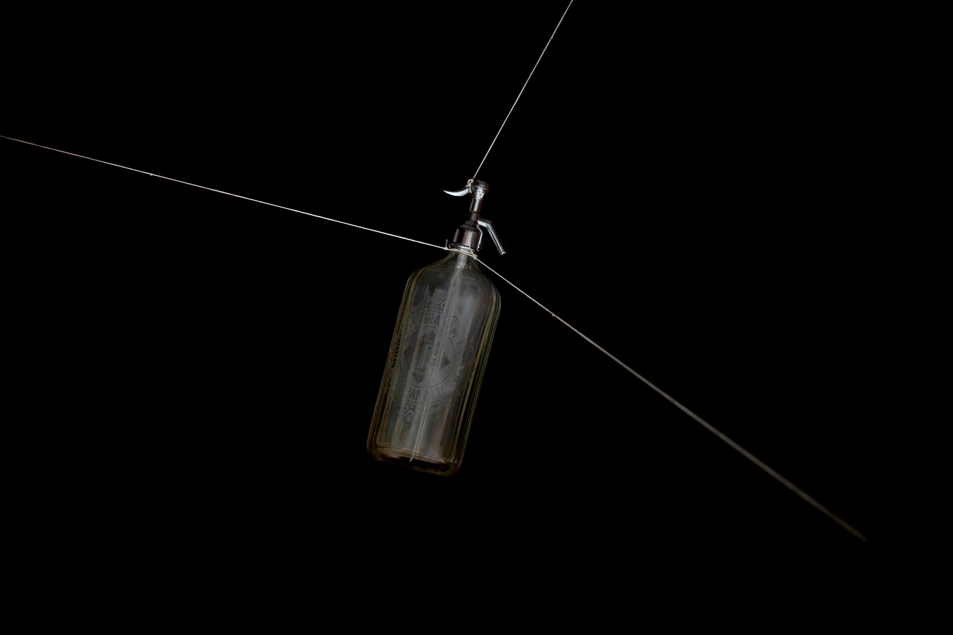 Soda syphon bottle hanging by strings on a black background