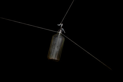 Soda syphon bottle hanging by strings on a black background