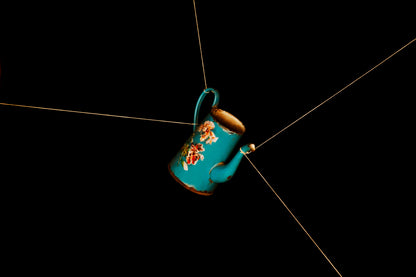 Blue toleware jug hanging from a string against a black background