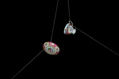 Tea cup and saucer hanging from string against a black background