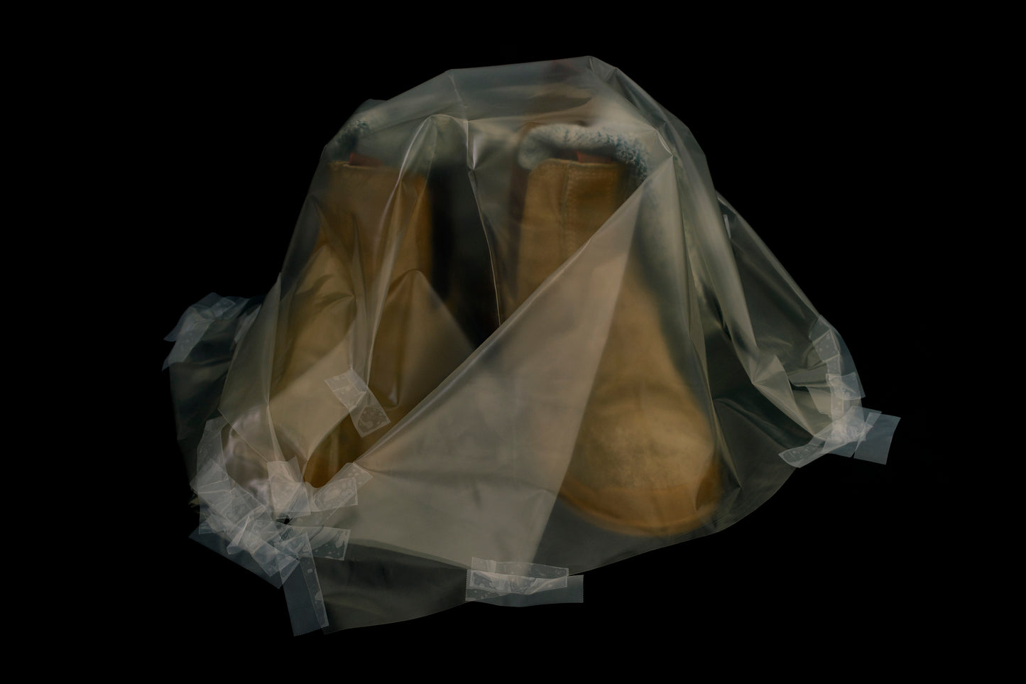 Pair of brown shoes wrapped in clear plastic on a black background
